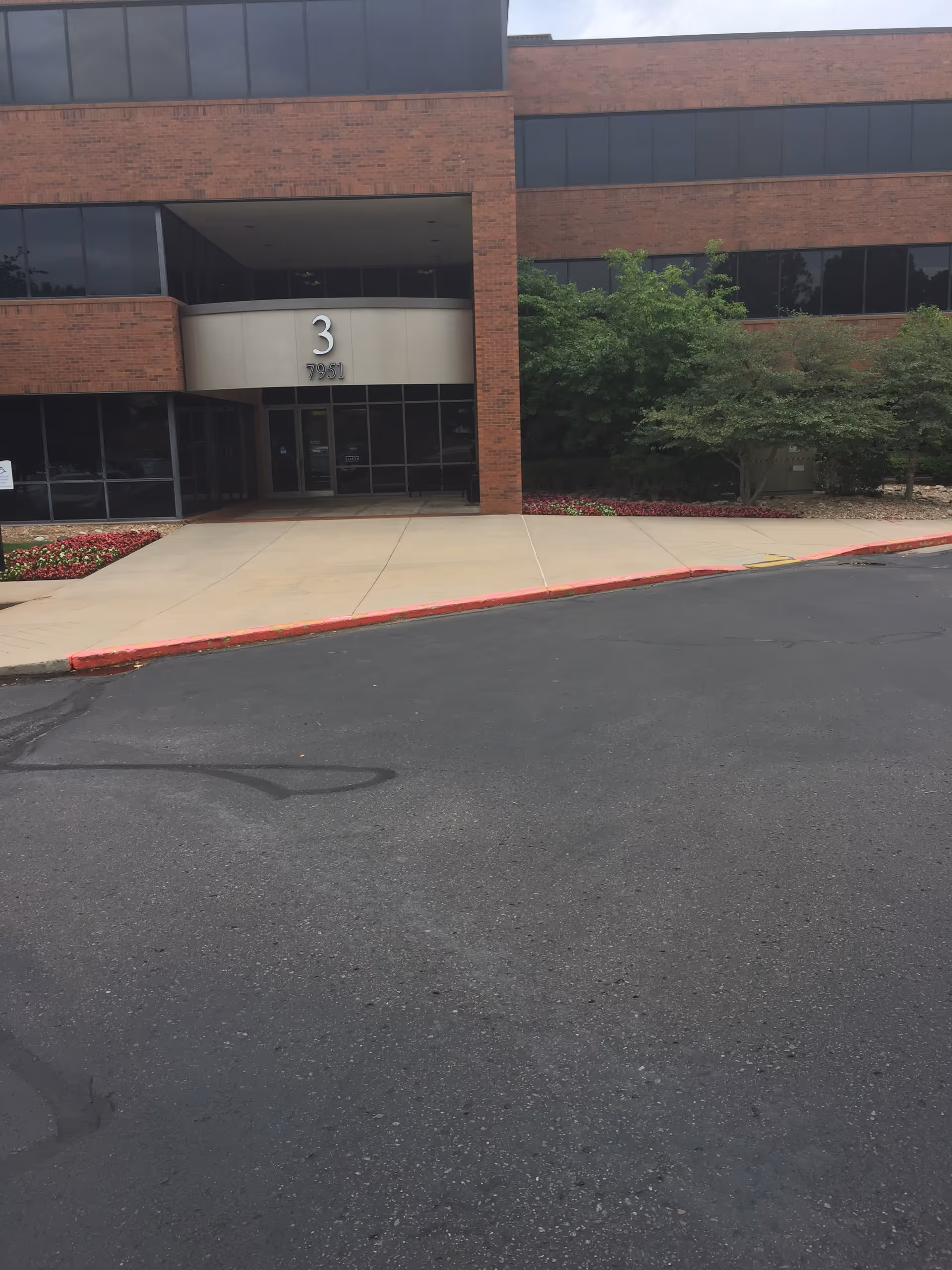 Exterior view of a brick building front with glass doors and landscaping.