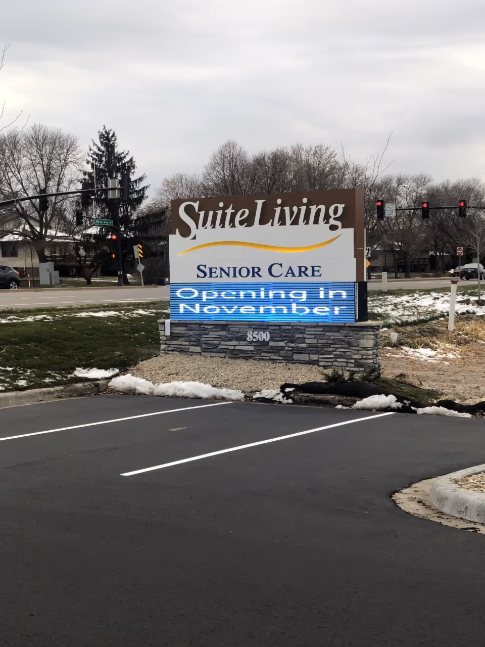 Outdoor sign for Suite Living Senior Care on a stone base beside a parking lot.