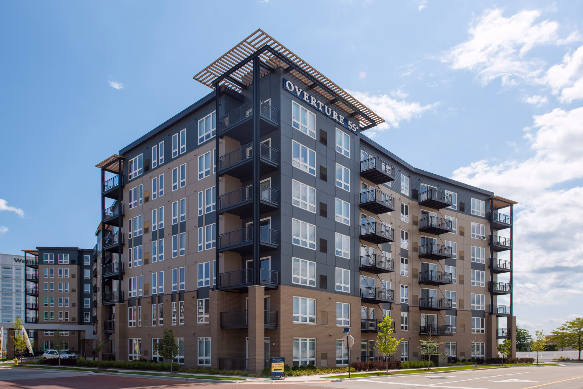 Exterior front view of the multi-story Overture 55+ apartment building with balconies under a blue sky.