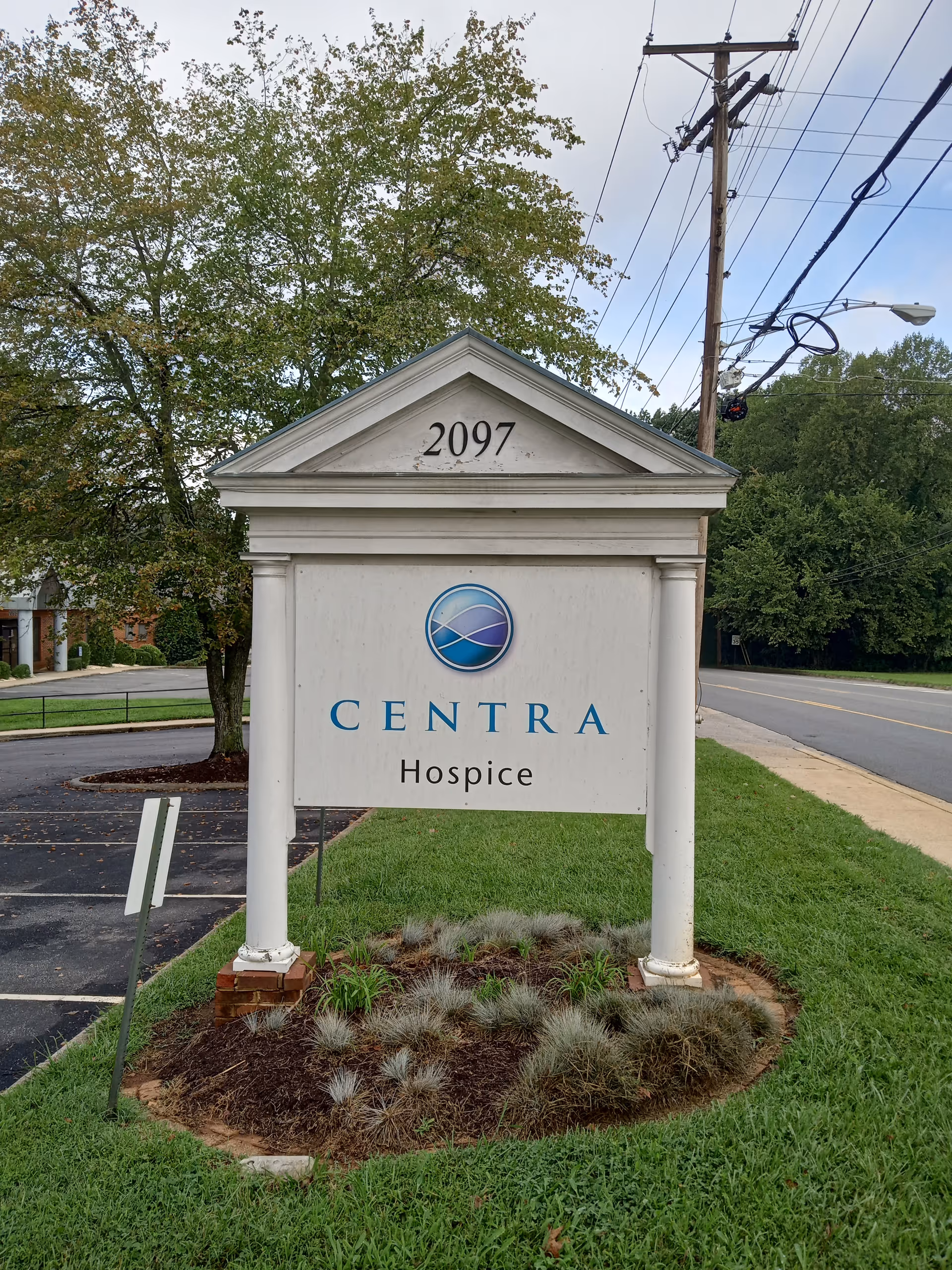 A white Centra Hospice sign on a landscaped lawn beside a road.