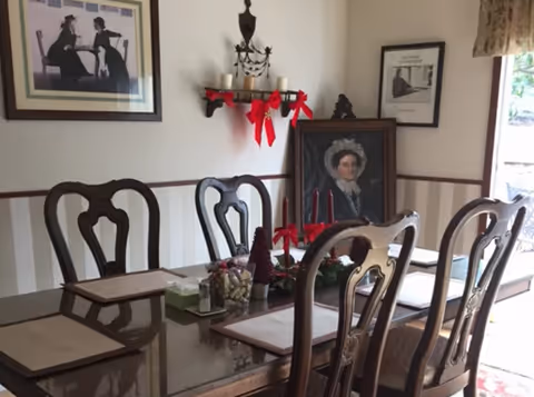 Dining room with glass table, wooden chairs, and framed wall art.