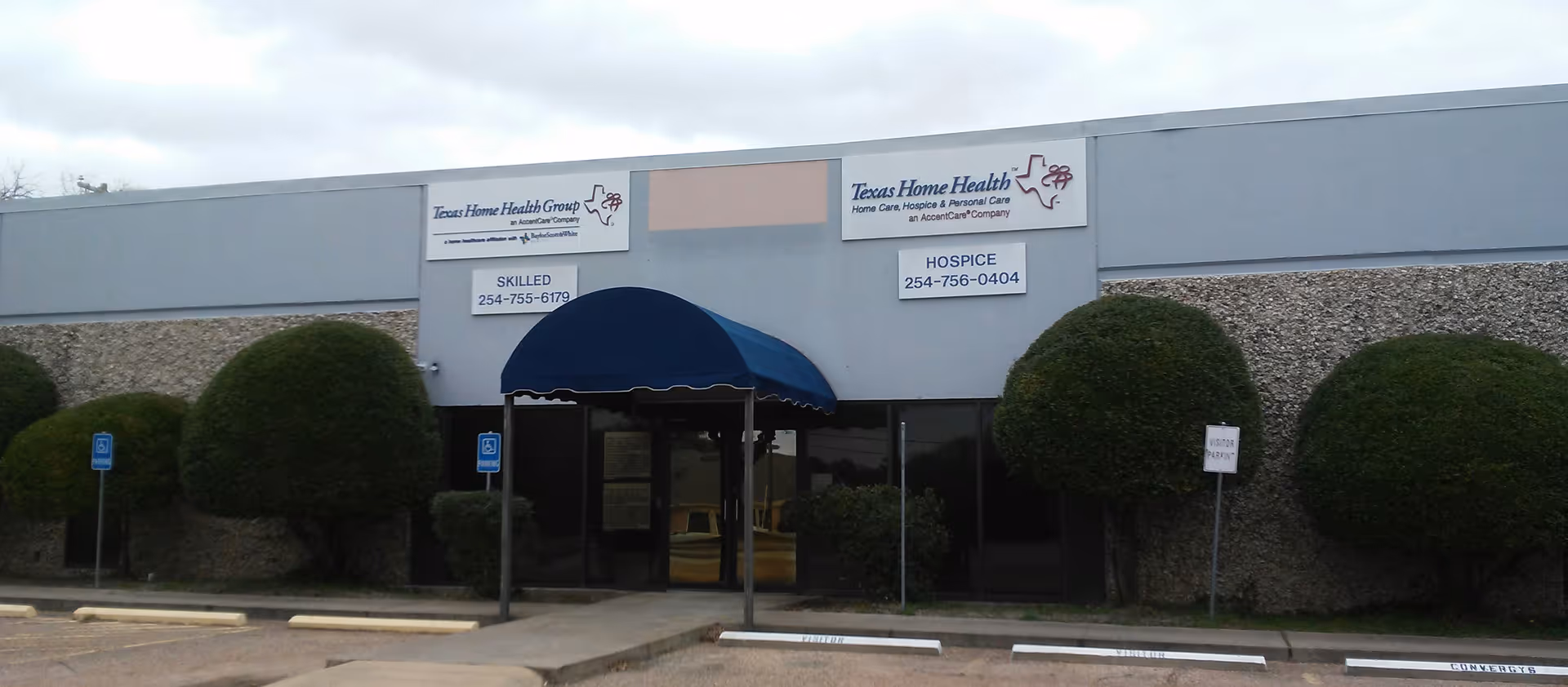 Front view of a medical facility with a blue canopy and trimmed shrubs