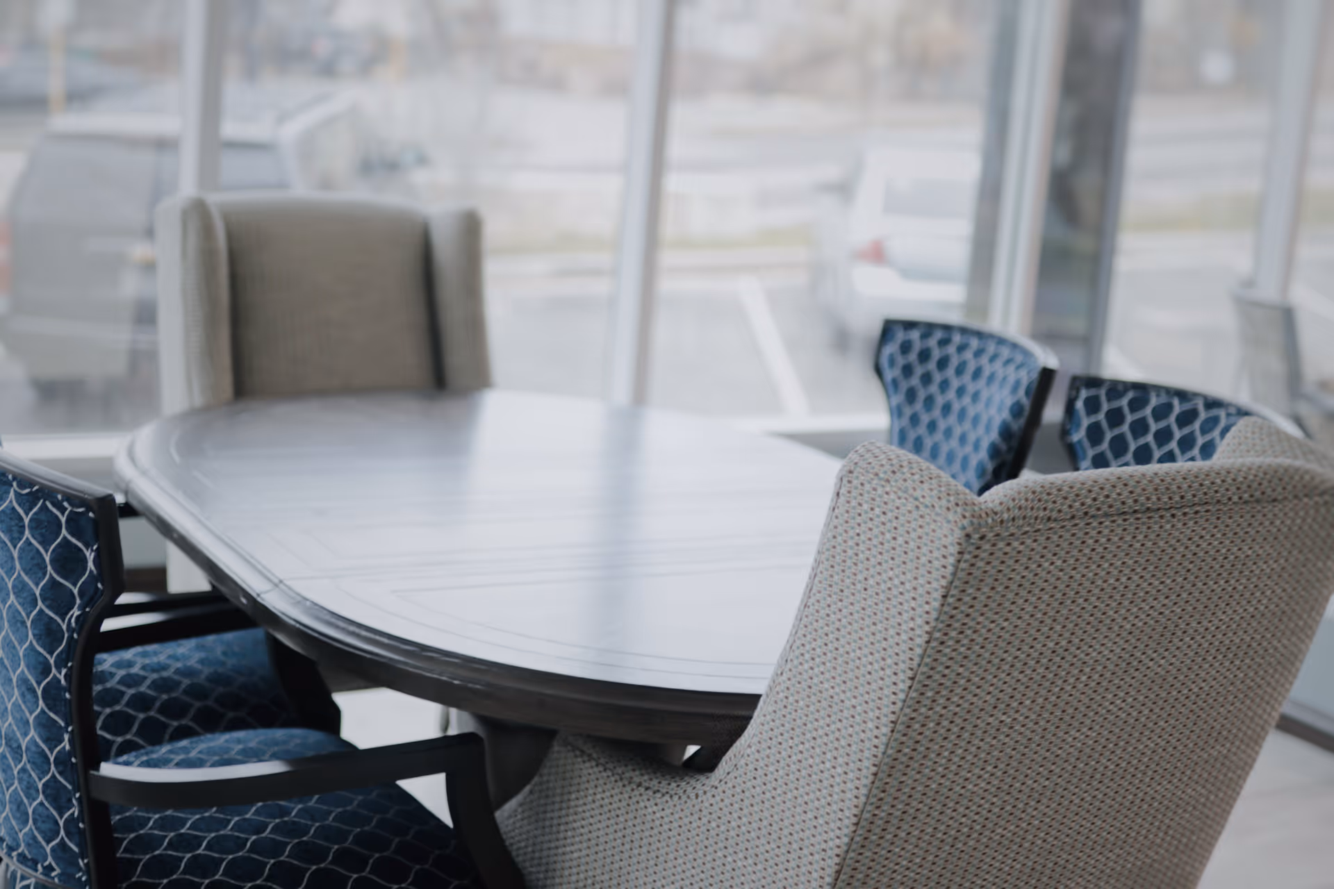 Round dining table with upholstered chairs in a bright, windowed dining area.