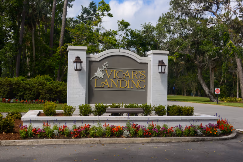 Entrance sign reading Vicar's Landing surrounded by colorful flowers and trees.