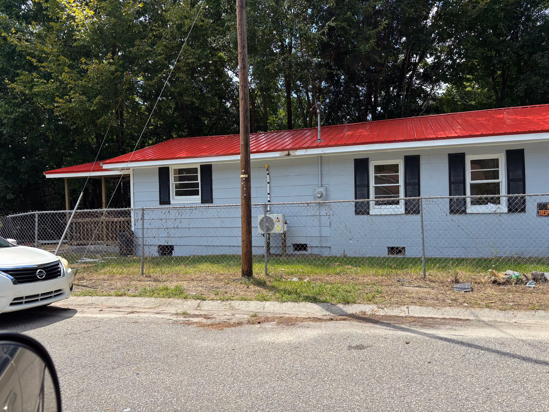 A single-story blue building with a red metal roof, chain-link fence, and surrounding trees.
