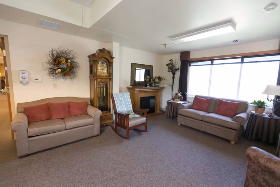 Living room in West Bend Health and Rehabilitation with sofas, clock, fireplace, and a large window