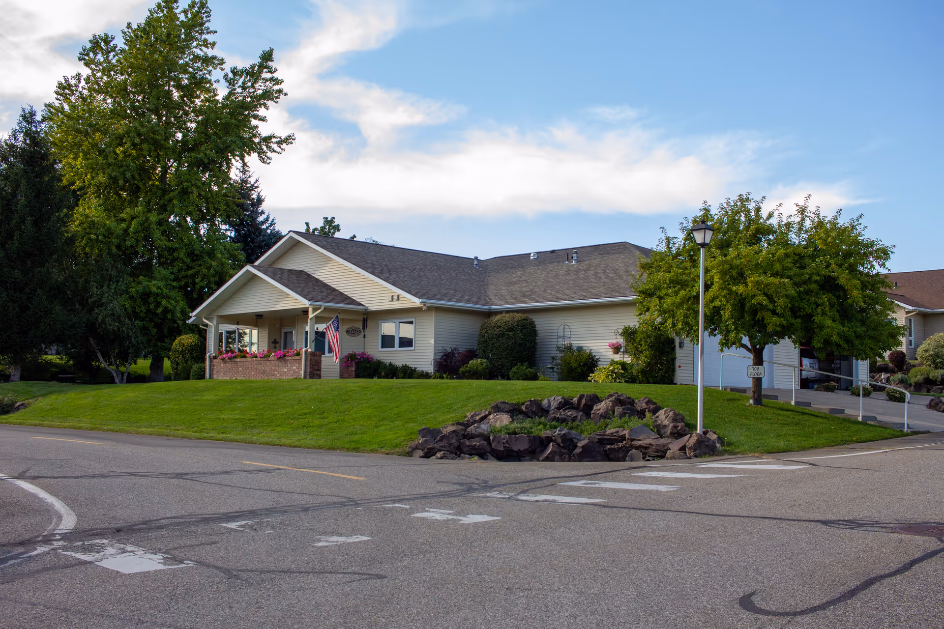 Single story senior living building with front entrance, manicured lawn, flag, and rock garden.
