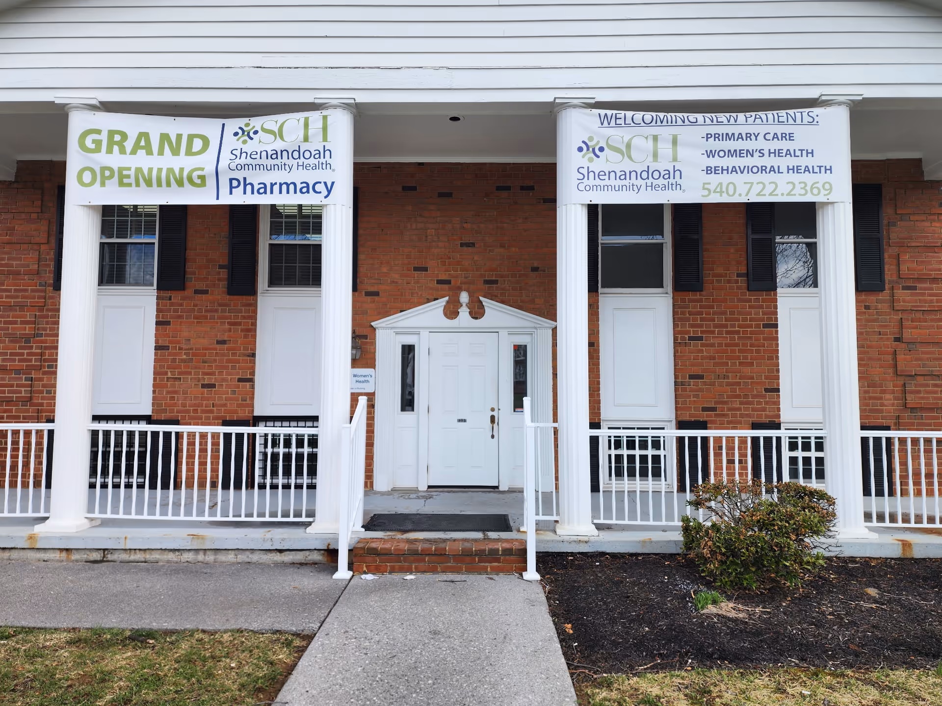 Brick building with white columns and banners advertising grand opening.