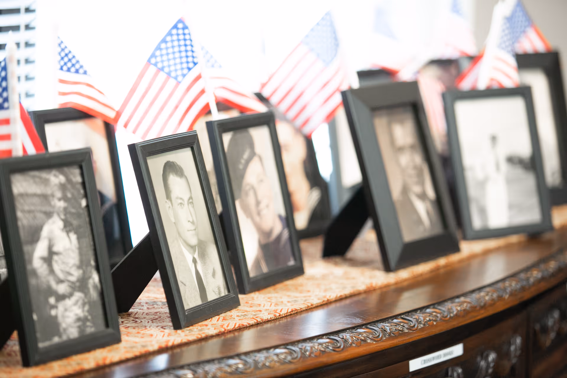 A row of framed black-and-white portrait photos with small American flags placed behind them on a wooden table.