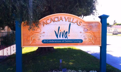 A wooden Acacia Villas sign with Viva! A Celebration of Senior Living, mounted on blue posts.