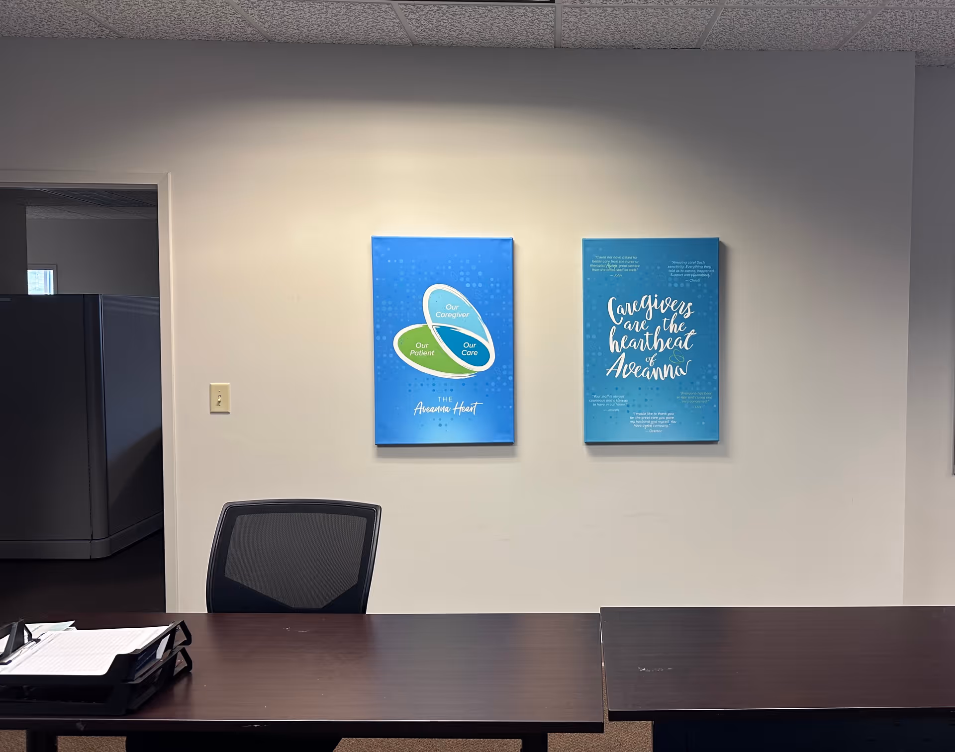 Office reception area with two blue posters on a light wall and a dark desk.