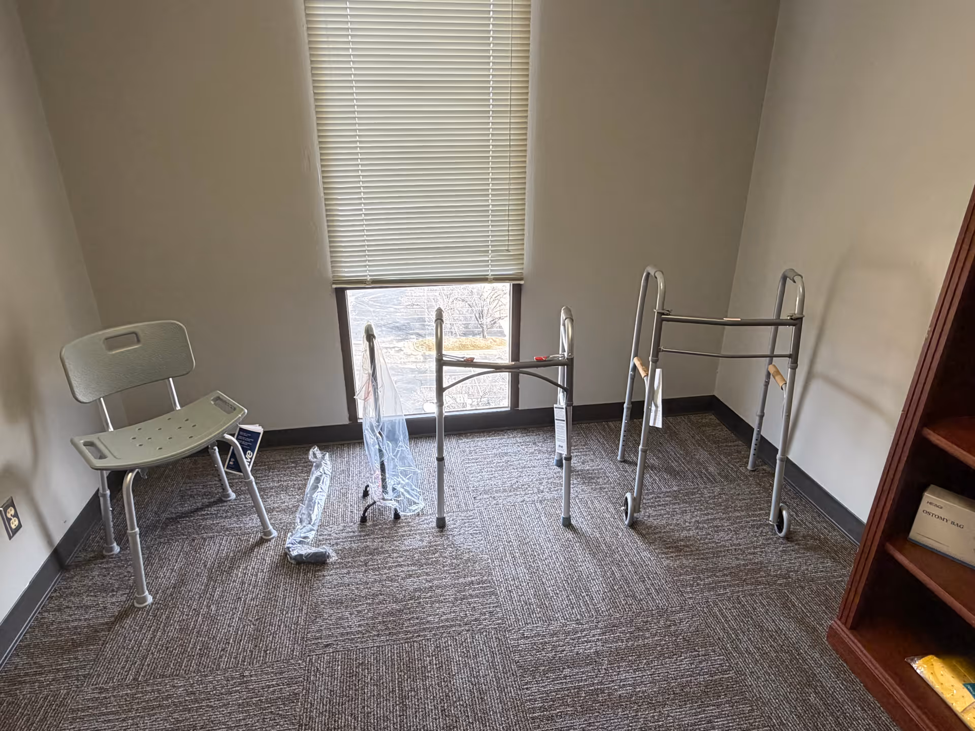 Small interior room with window blinds and mobility aids like walkers and a chair.