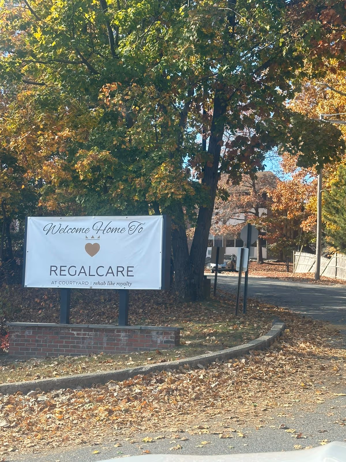 Tree-lined exterior street with a RegalCare sign and autumn leaves.