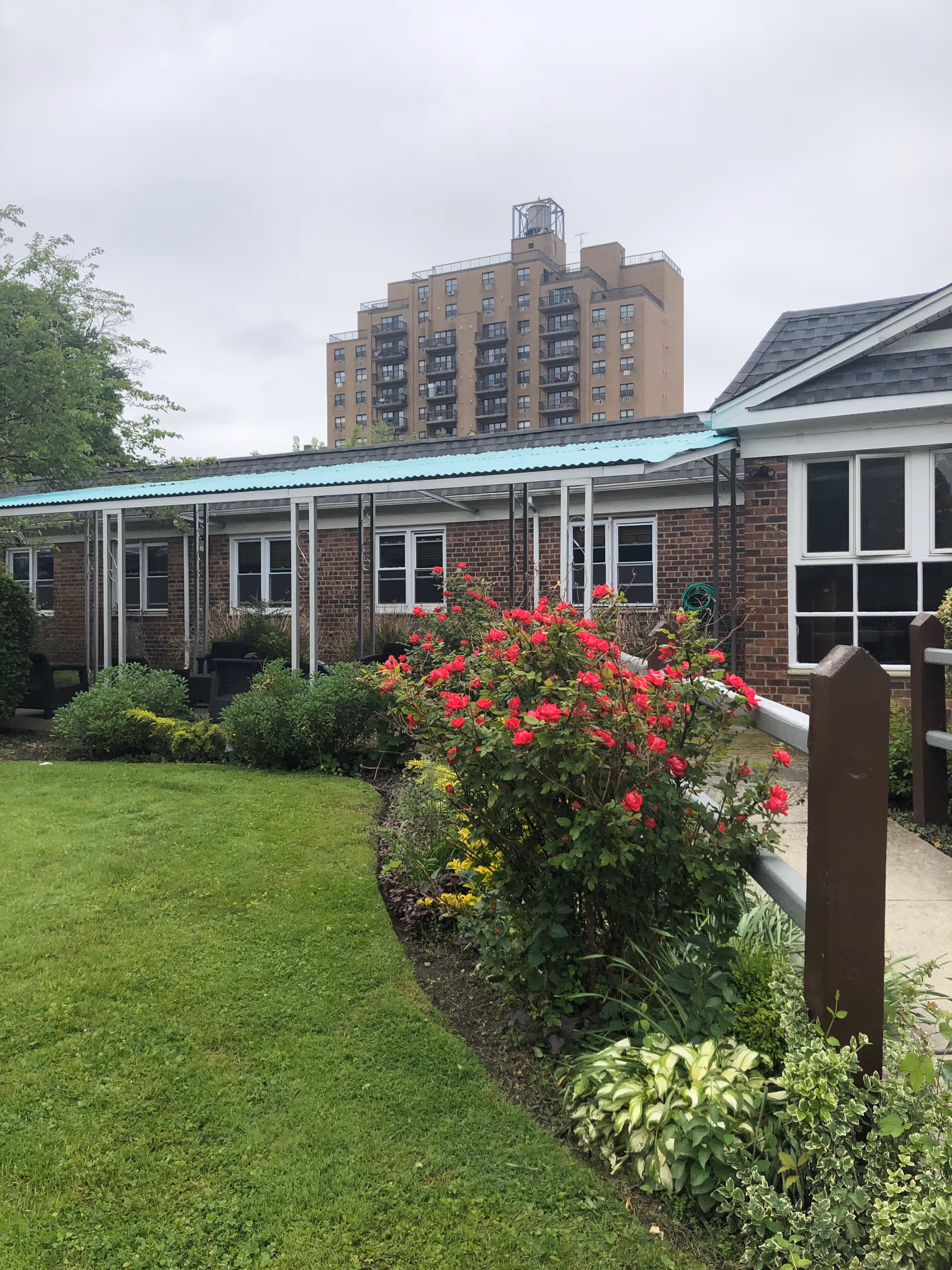 Brick building with a covered walkway, rose bushes, and a manicured lawn in foreground.