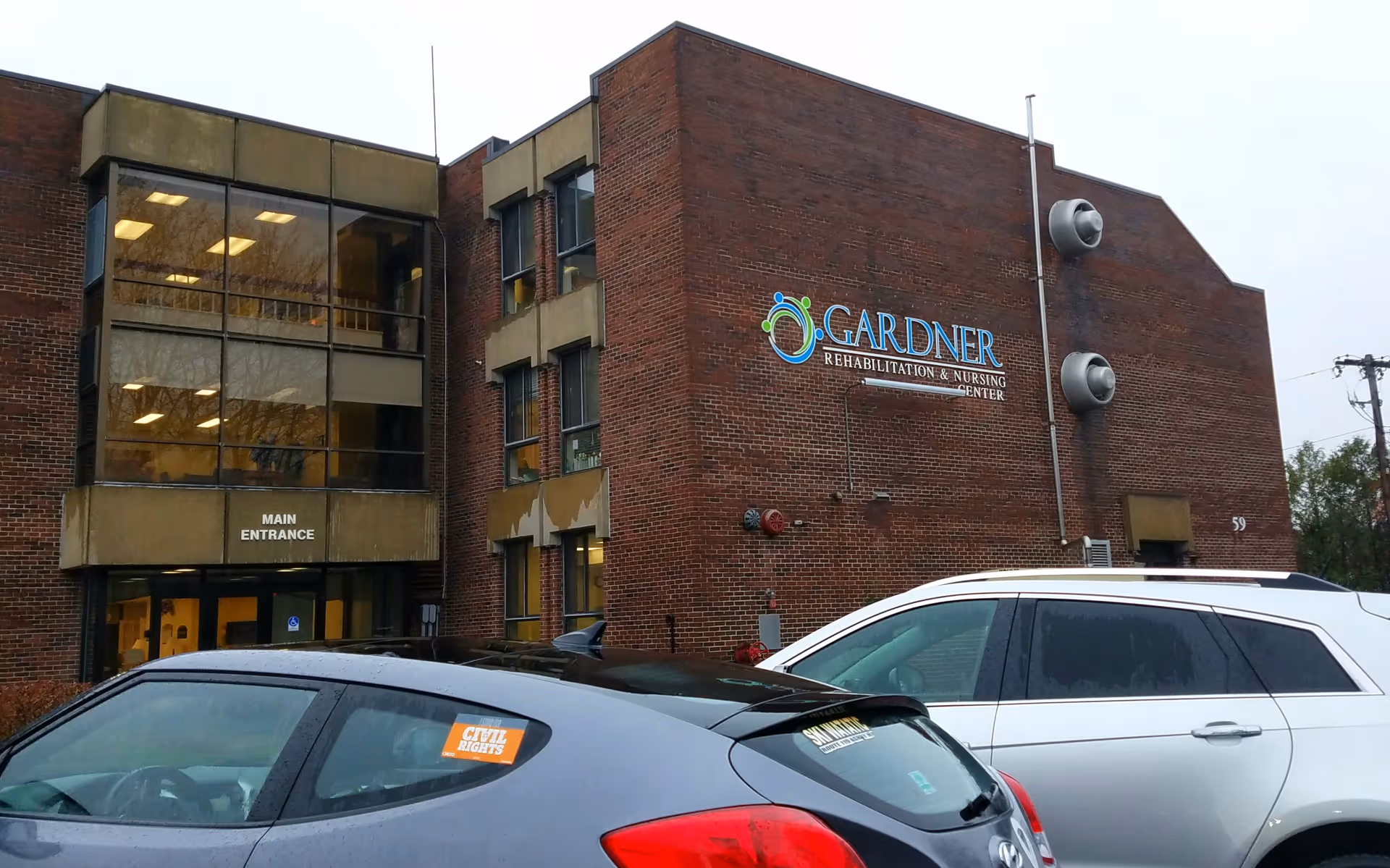 Exterior of Gardner Rehabilitation & Nursing Center, brick building with sign and parked cars.