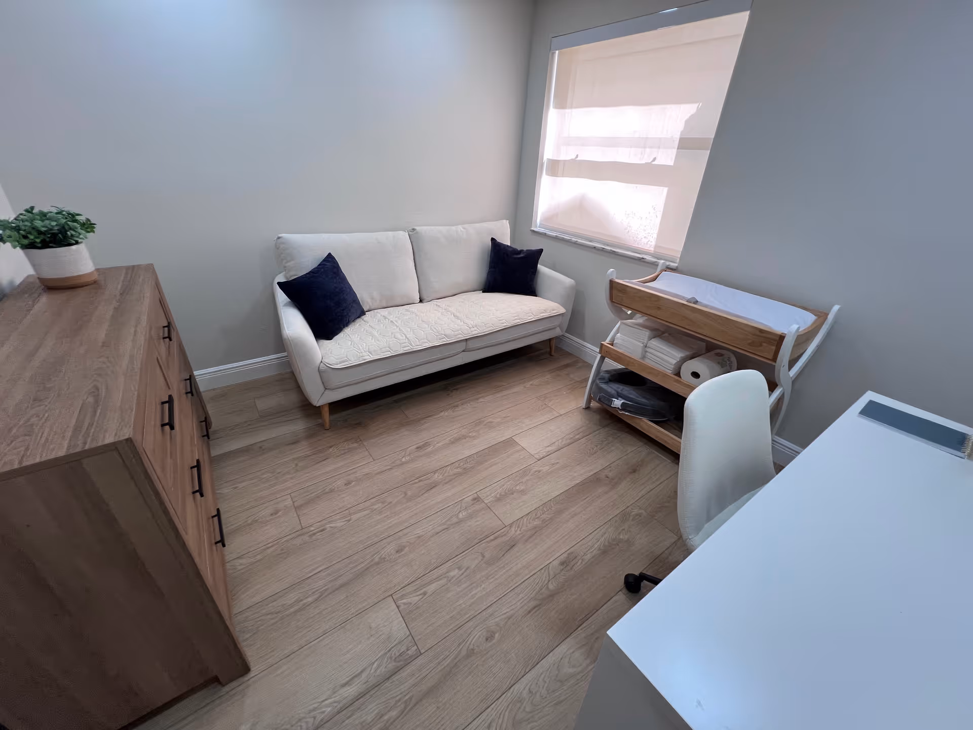 Small modern living area with a white sofa, wooden dresser, and desk.