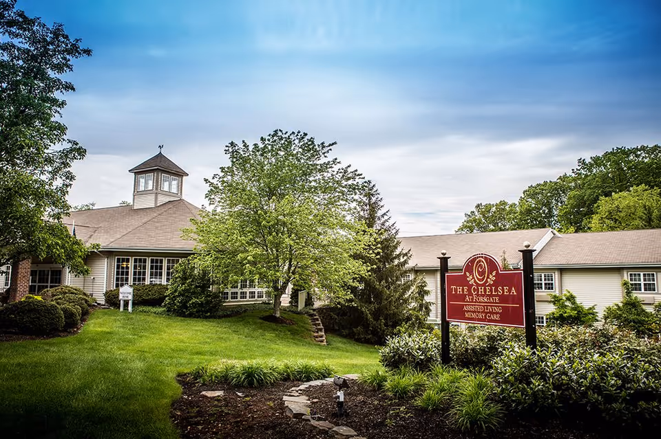 Exterior view of a senior living facility with lawn, trees, and sign.