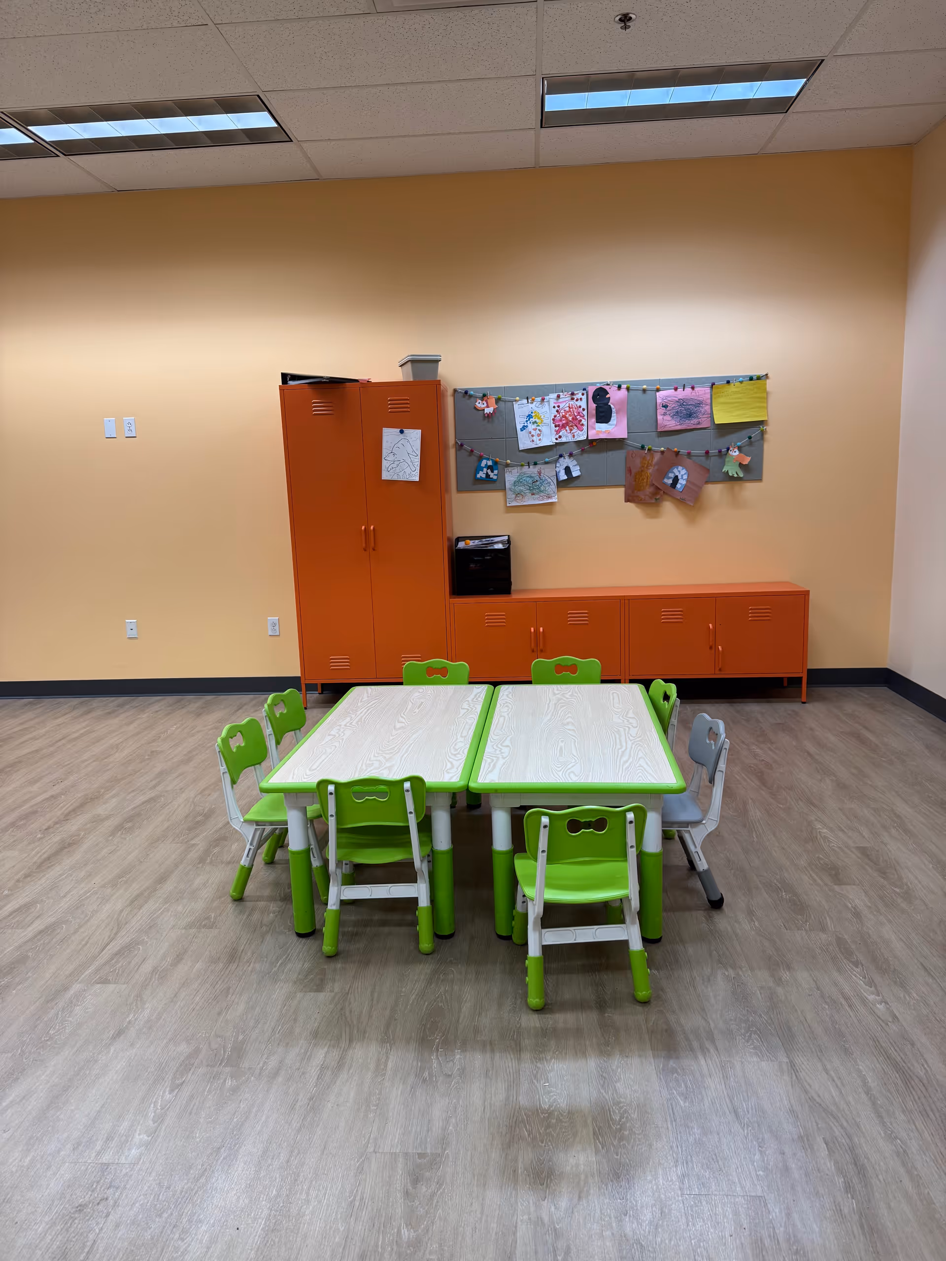 Bright orange cabinets and green children's tables in an activity room.