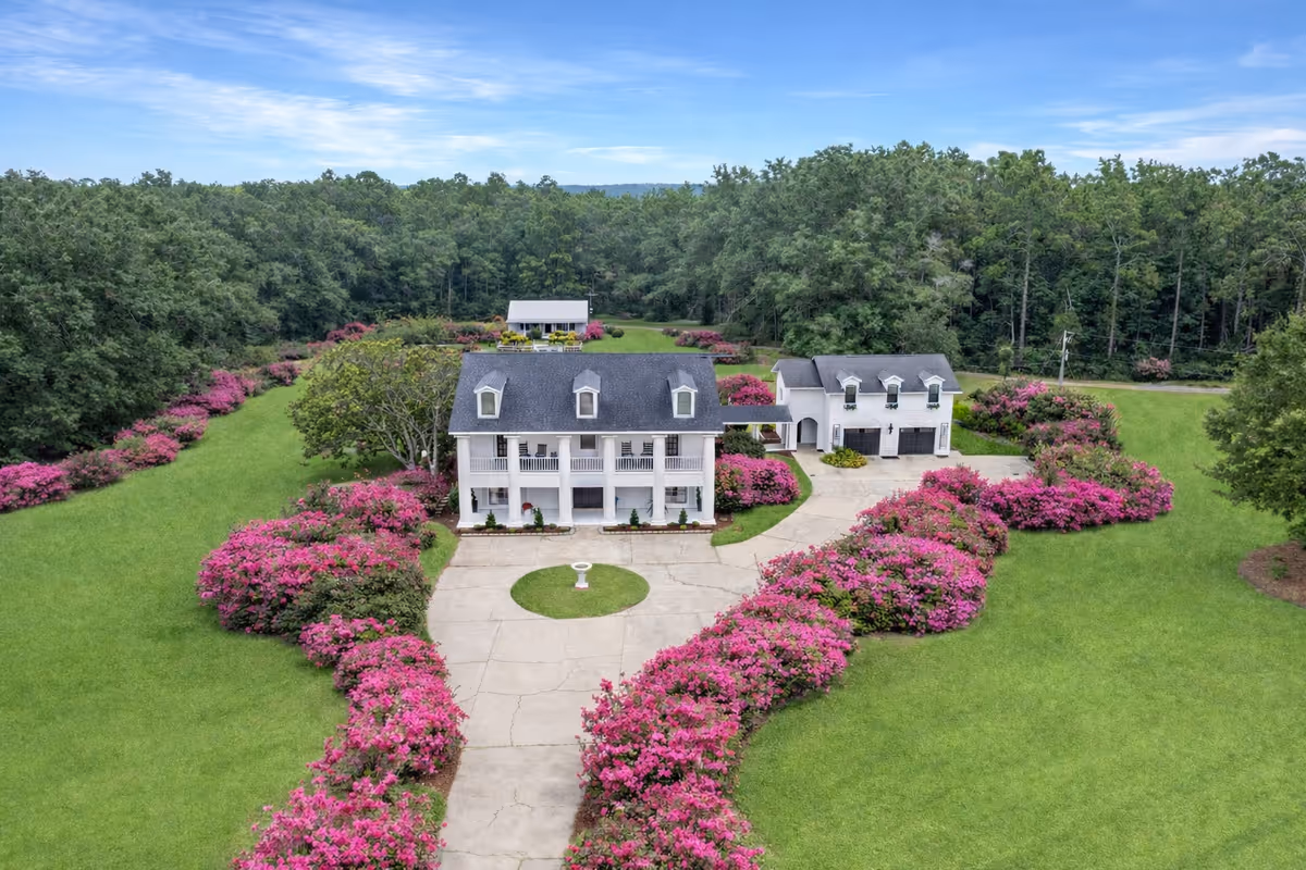 Large white building front with circular driveway and pink flowering shrubs.