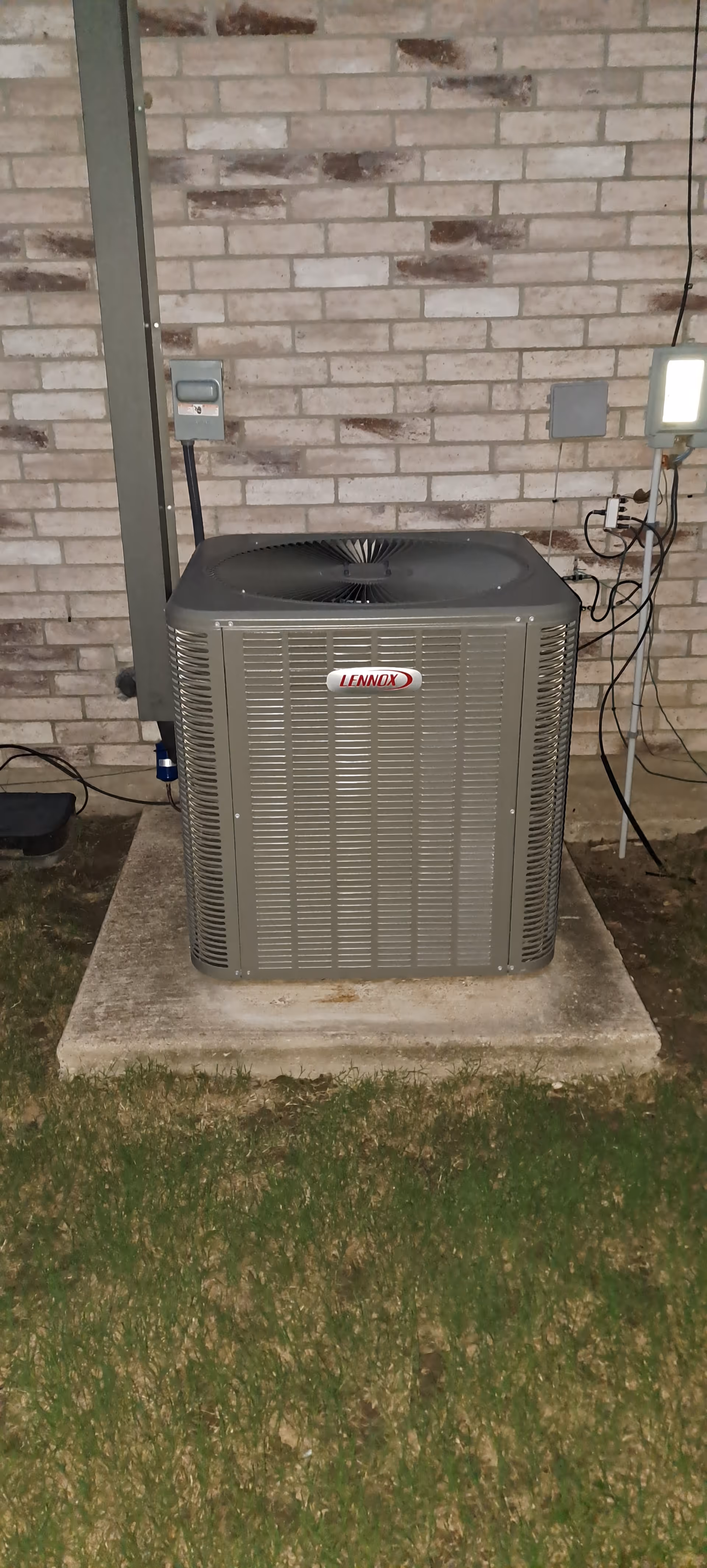 Exterior Lennox air conditioning unit on concrete pad beside brick wall.