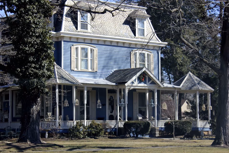 Large blue Victorian-style house with wraparound porch and hanging lanterns.