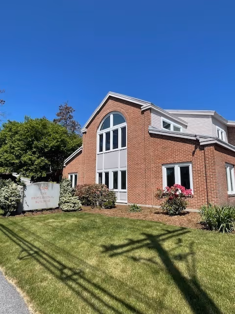 Brick senior living building with large arched windows, well-kept lawn, and sign by entrance.