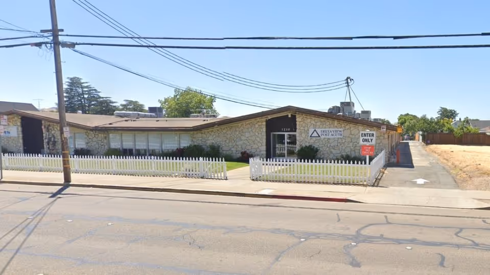 Single-story stone building with white picket fence and Delta View Post Acute sign.