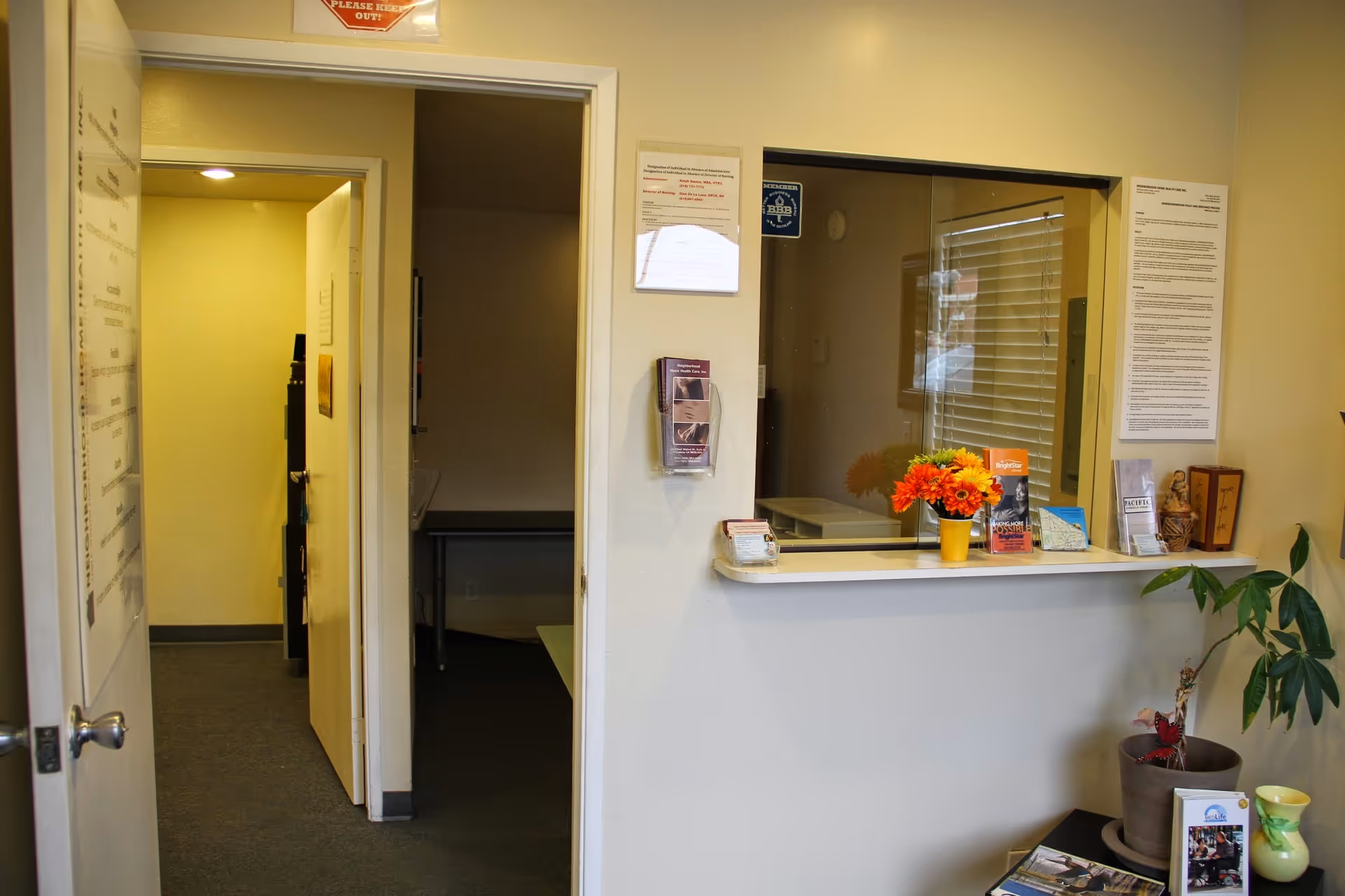 Reception window, brochures, flowers, and a potted plant in a clinic lobby.