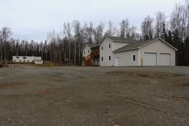 Exterior view of a beige senior living building with an outdoor staircase and gravel yard.