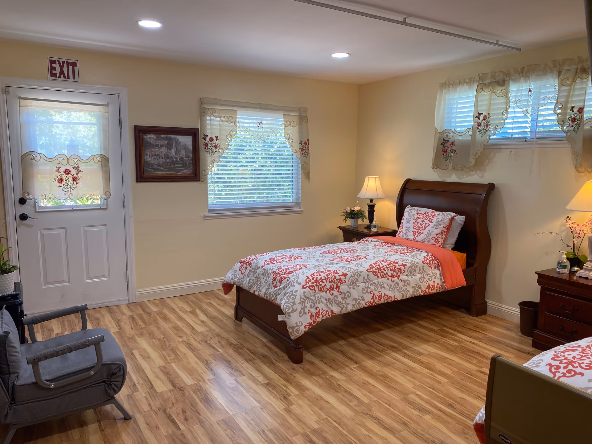 Bright bedroom with a wooden bed, nightstands, lamps, and patterned curtains in a senior home.