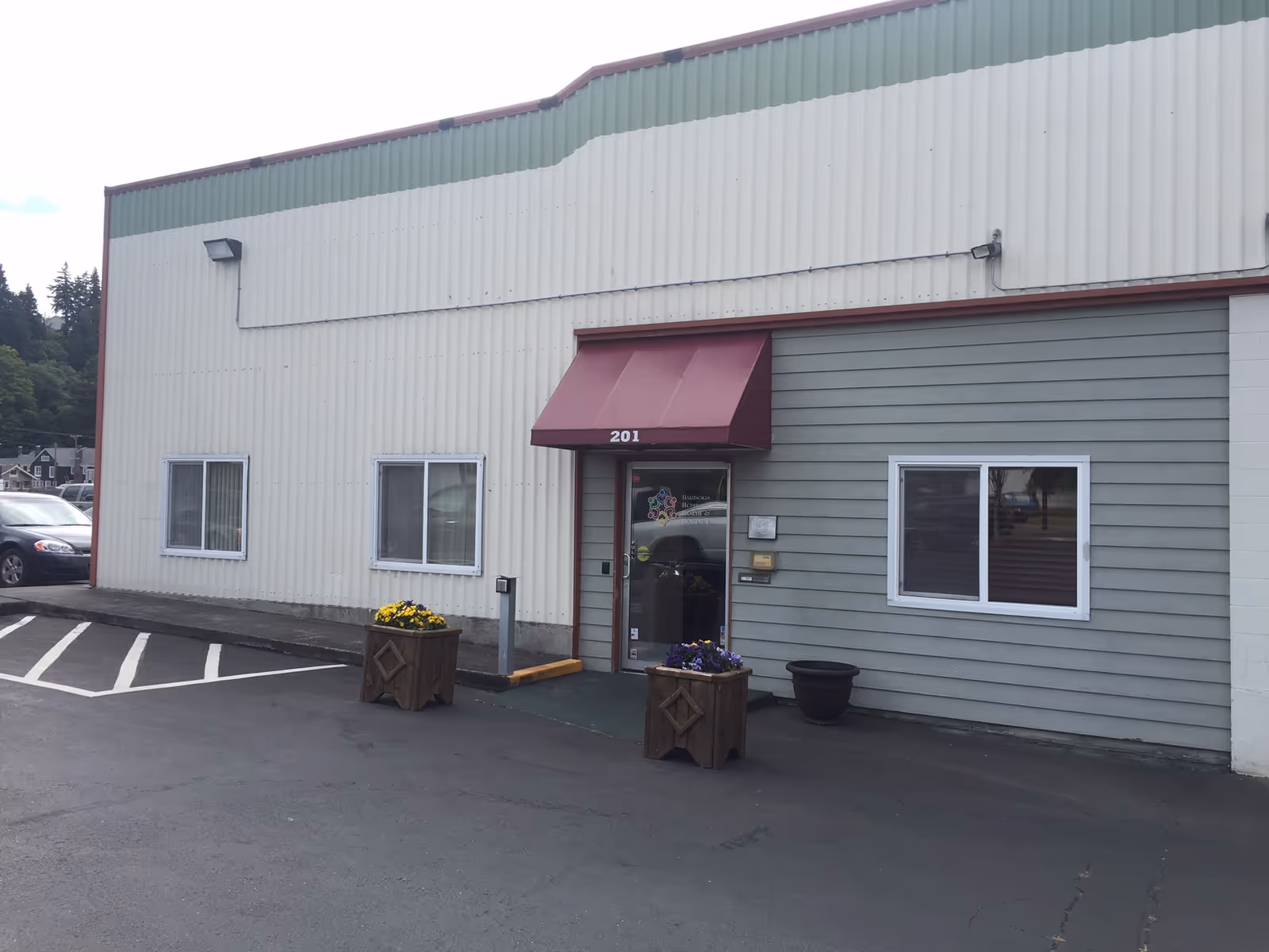 Exterior view of a facility building with maroon awning, parking lot, and flower planters.