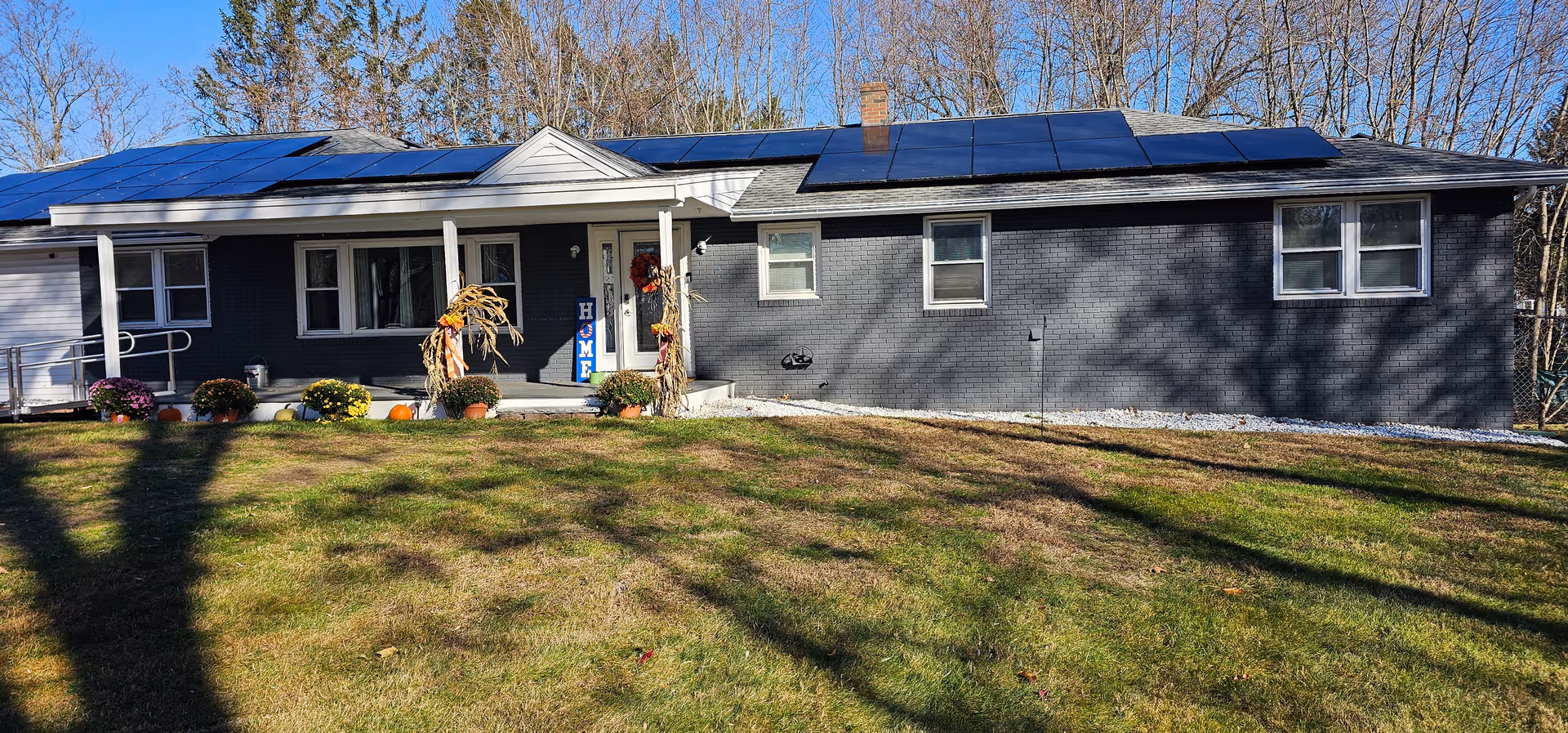 Exterior view of a single-story dark-gray building with solar panels and autumn decorations at the entrance.