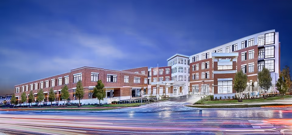 Nighttime front view of a multi-story brick senior living facility with illuminated windows and a drive-up entrance.