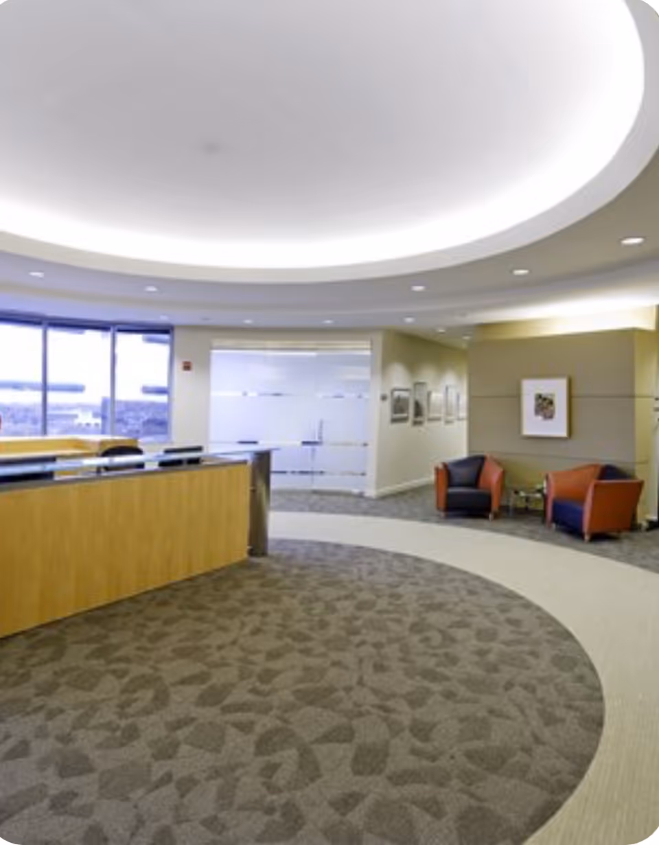 Modern lobby with curved ceiling, reception desk, and orange chairs.