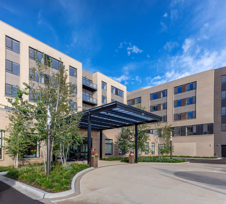 Modern senior living building with a glass entrance and landscaped courtyard under a blue sky