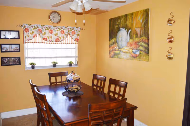 Yellow dining room with a wooden table, six chairs, window, and wall art.