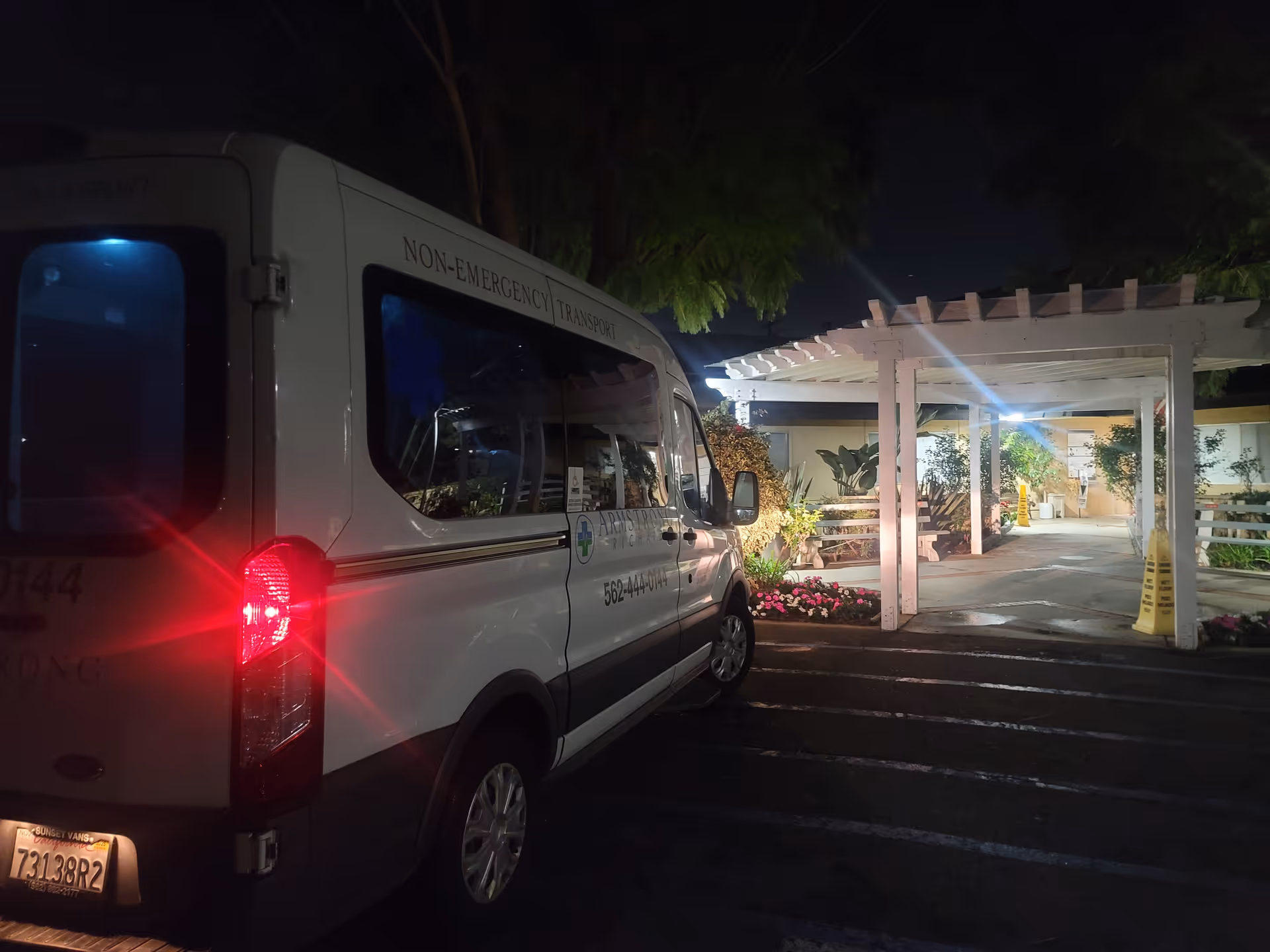 A white non-emergency transport van parked near the front entrance of a facility at night.