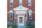 Front entrance of a red brick building labeled Loretto Home with wreath on the door.