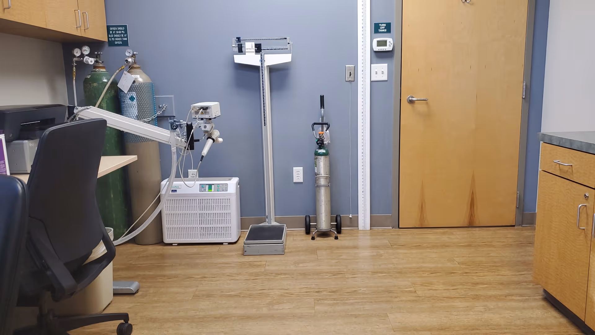 Medical equipment room with oxygen tanks, a standing scale, and cabinets.