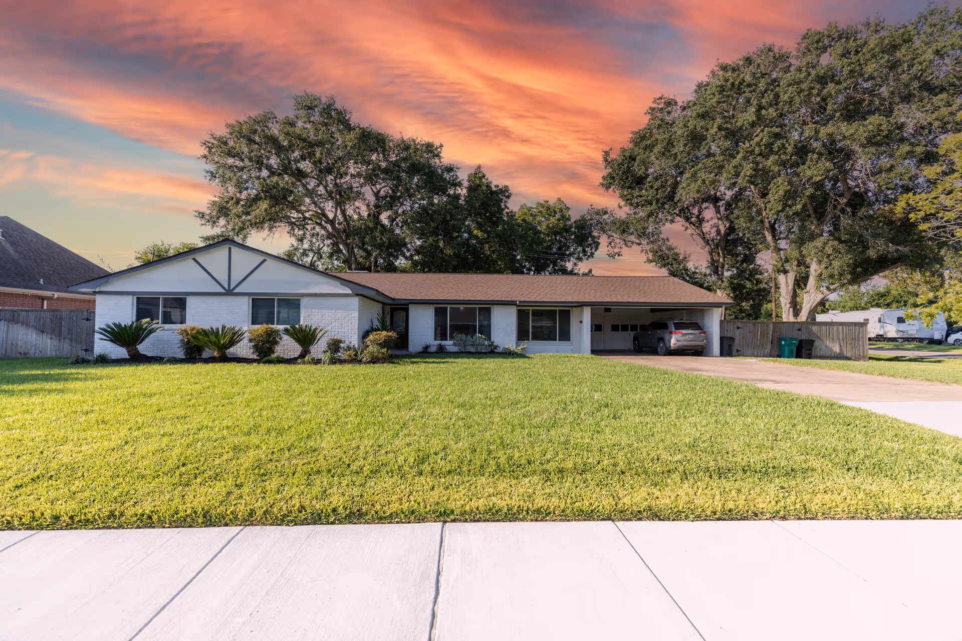 A single-story house with a front lawn, driveway, and carport at sunset.