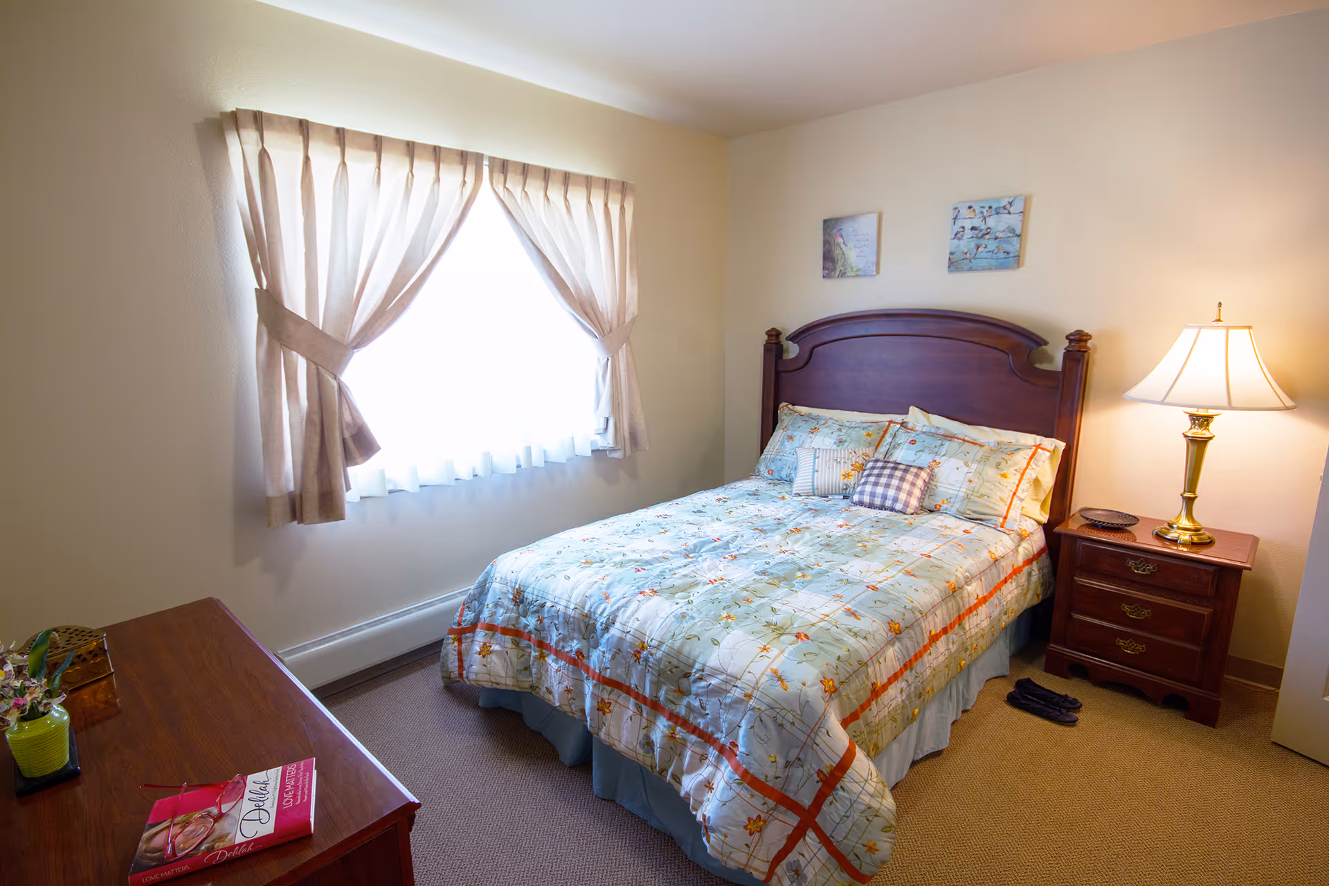 Cozy bedroom with a wooden headboard bed, nightstand, dresser, and curtained window.