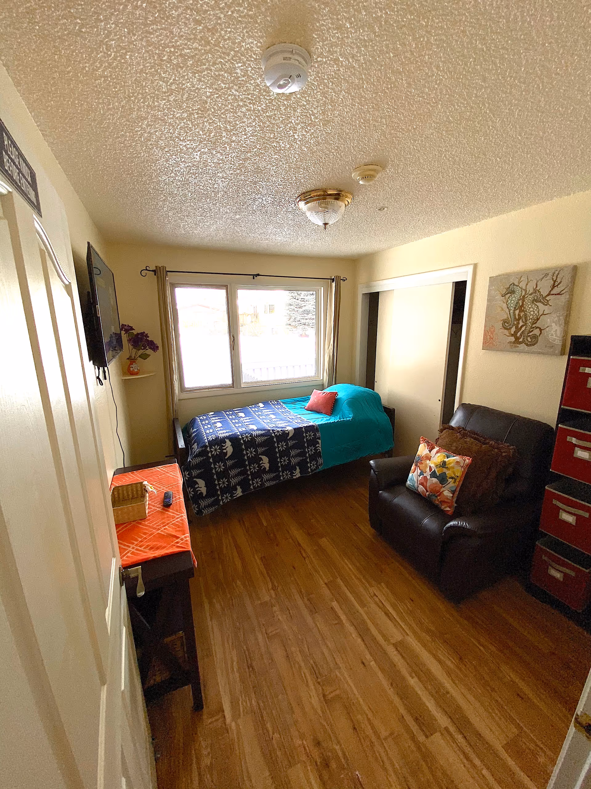 A compact senior living bedroom with a bed by the window and seating.