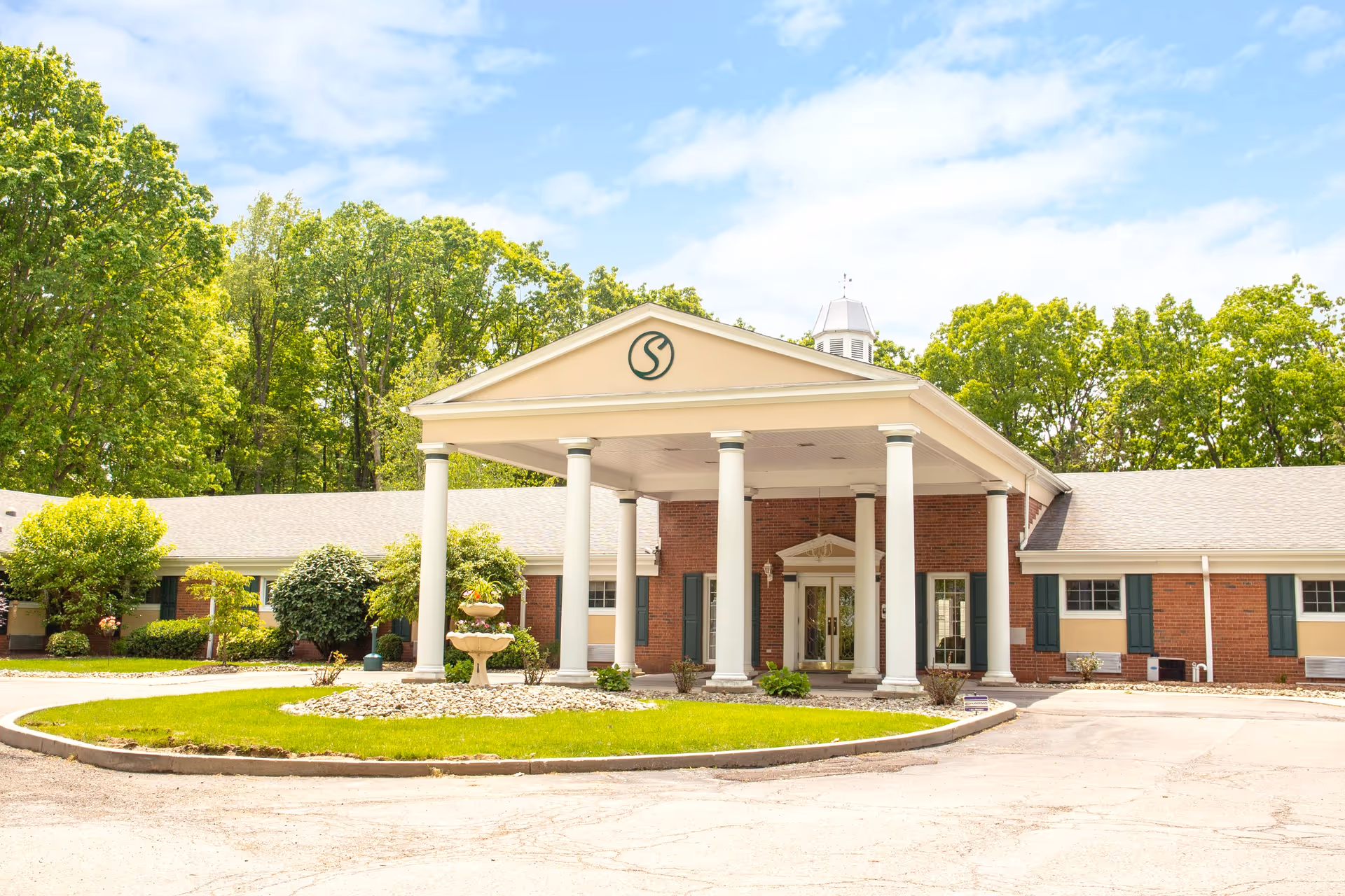 A single-story brick senior care center with a portico and white columns, surrounded by trees.