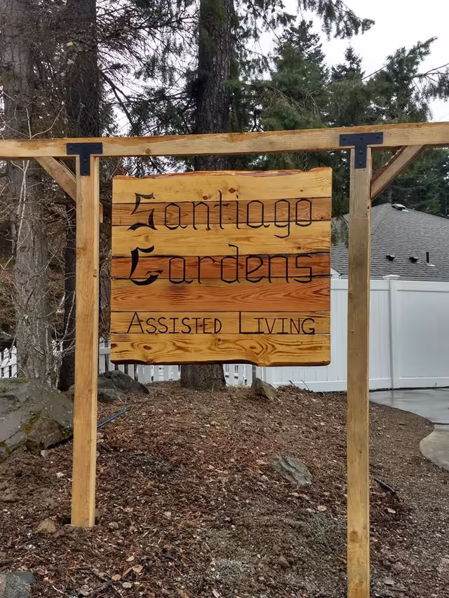 Wooden sign reading Santiago Gardens Assisted Living outdoors.