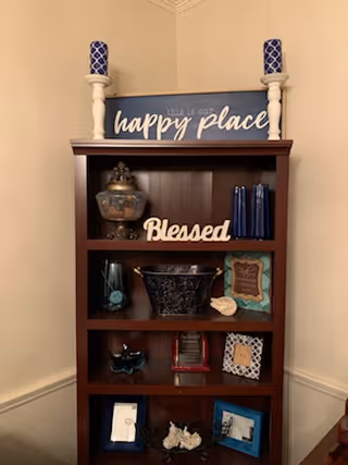 Wood bookshelf with decorative items and a blue Happy Place sign against beige wall