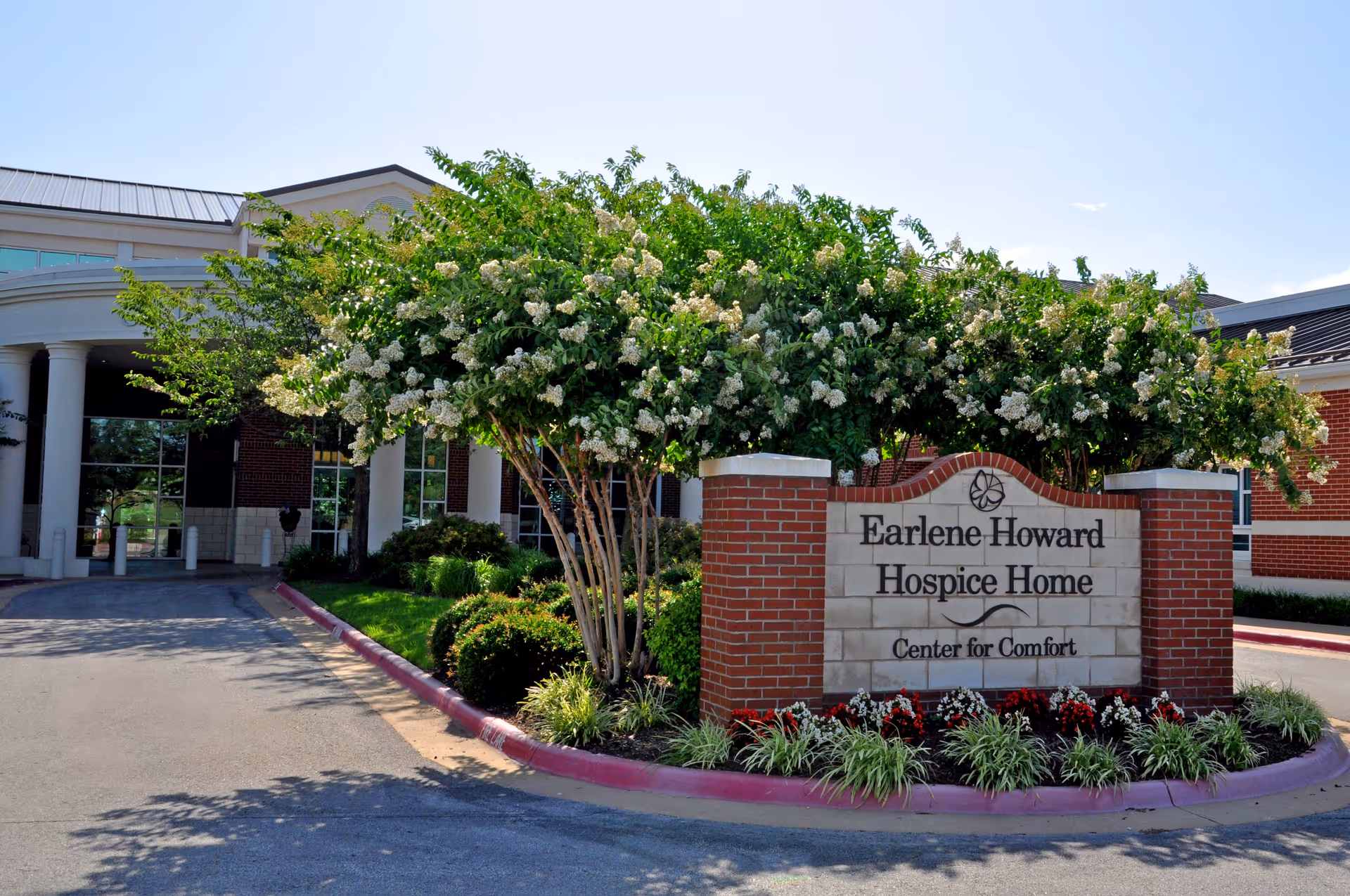 Exterior of a senior hospice facility with a brick entrance sign and landscaped surroundings.