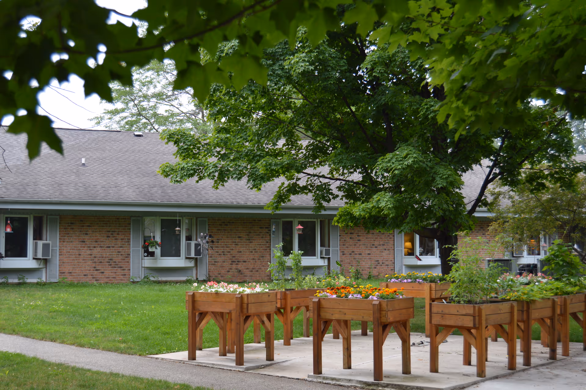 Brick senior living facility exterior with green lawn and wooden flower planters in foreground