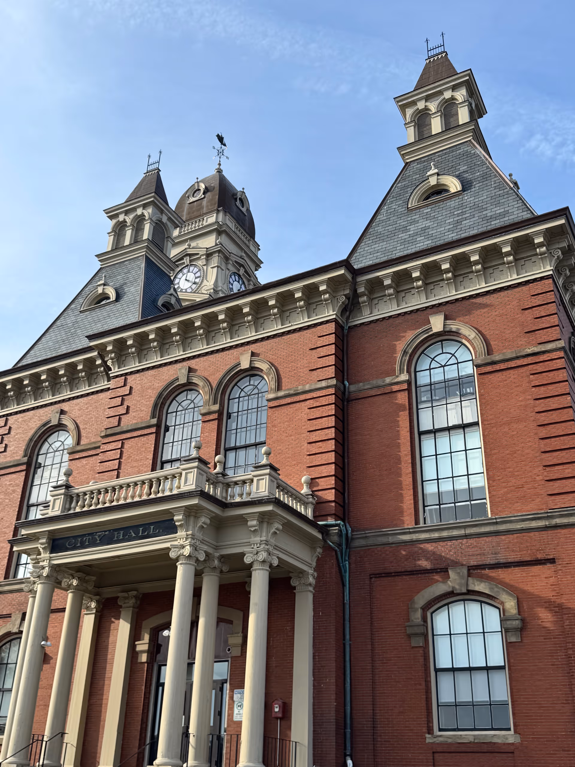 Red brick city hall with clock tower, arched windows, and a columned entrance
