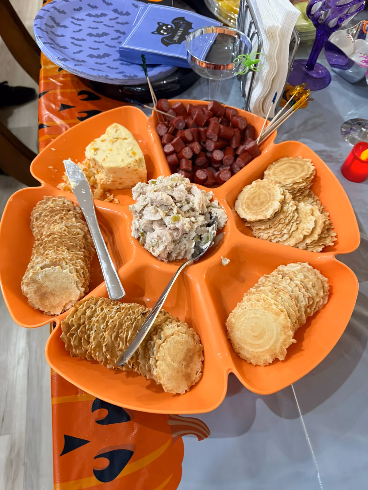 Orange flower shaped platter with crackers, cheese, meat cubes, and potato salad on a decorated table.