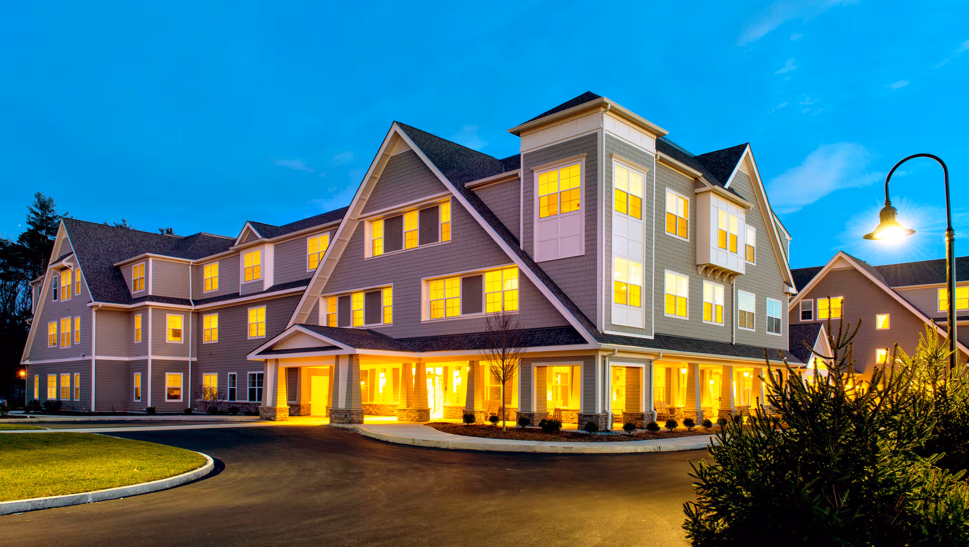 Exterior view of Stonebridge at Burlington, a multi-story senior living building glowing at dusk.
